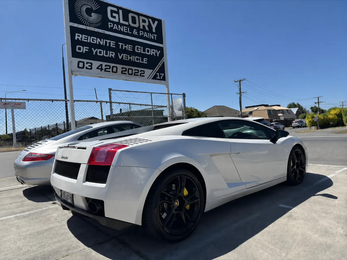 White Lamborghini Gallardo and Porsche outside the GLORY Panel & Paint sign, Christchurch